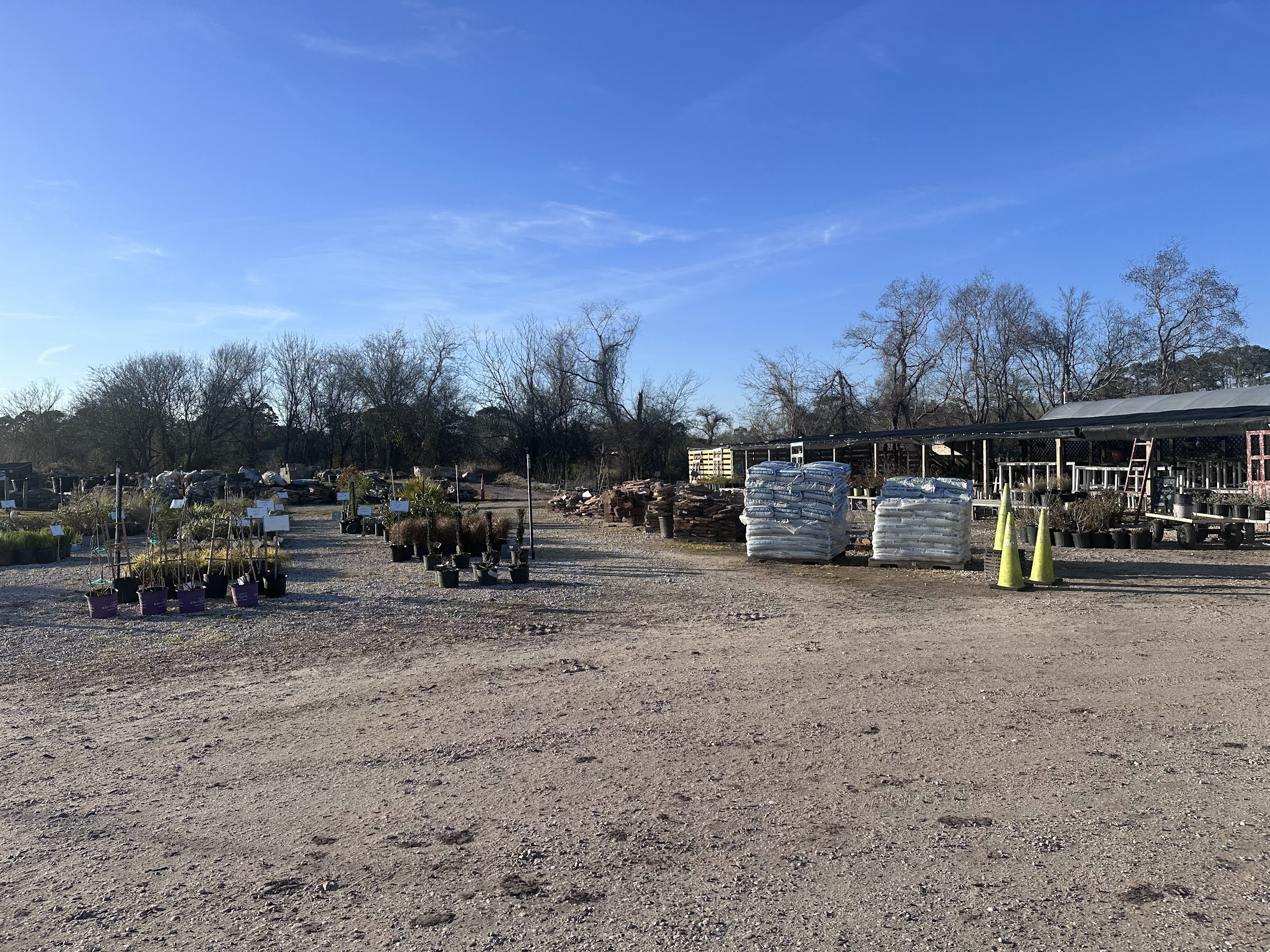 Nursery yard rows of potted shrubs and bagged materials under a clear Baytown sky